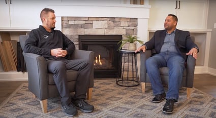 Two people sitting in chairs talking in front of a fireplace