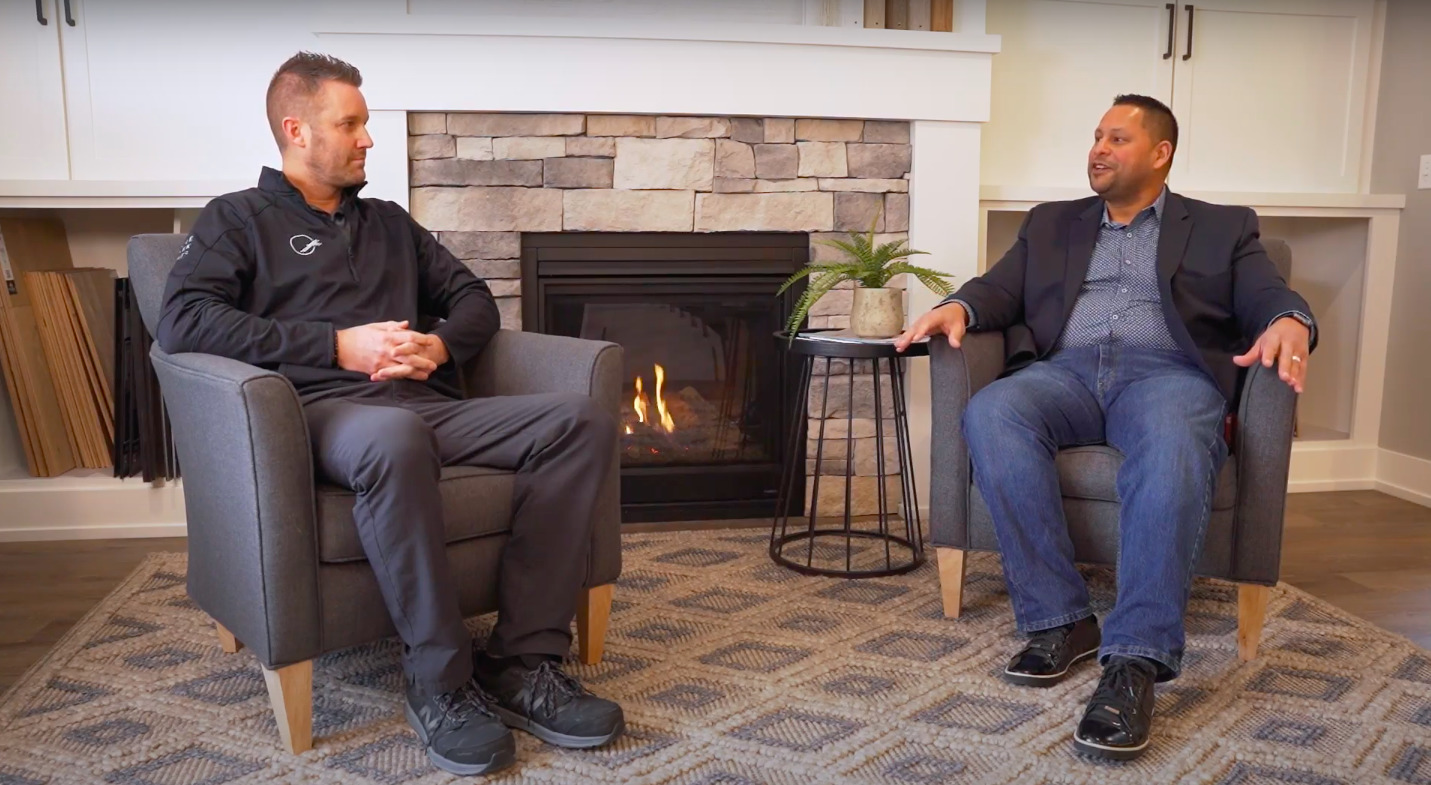 Two people sitting in chairs and talking in front of a fireplace